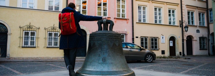 Girl with red backpack at the wishing bell in Warsaw
